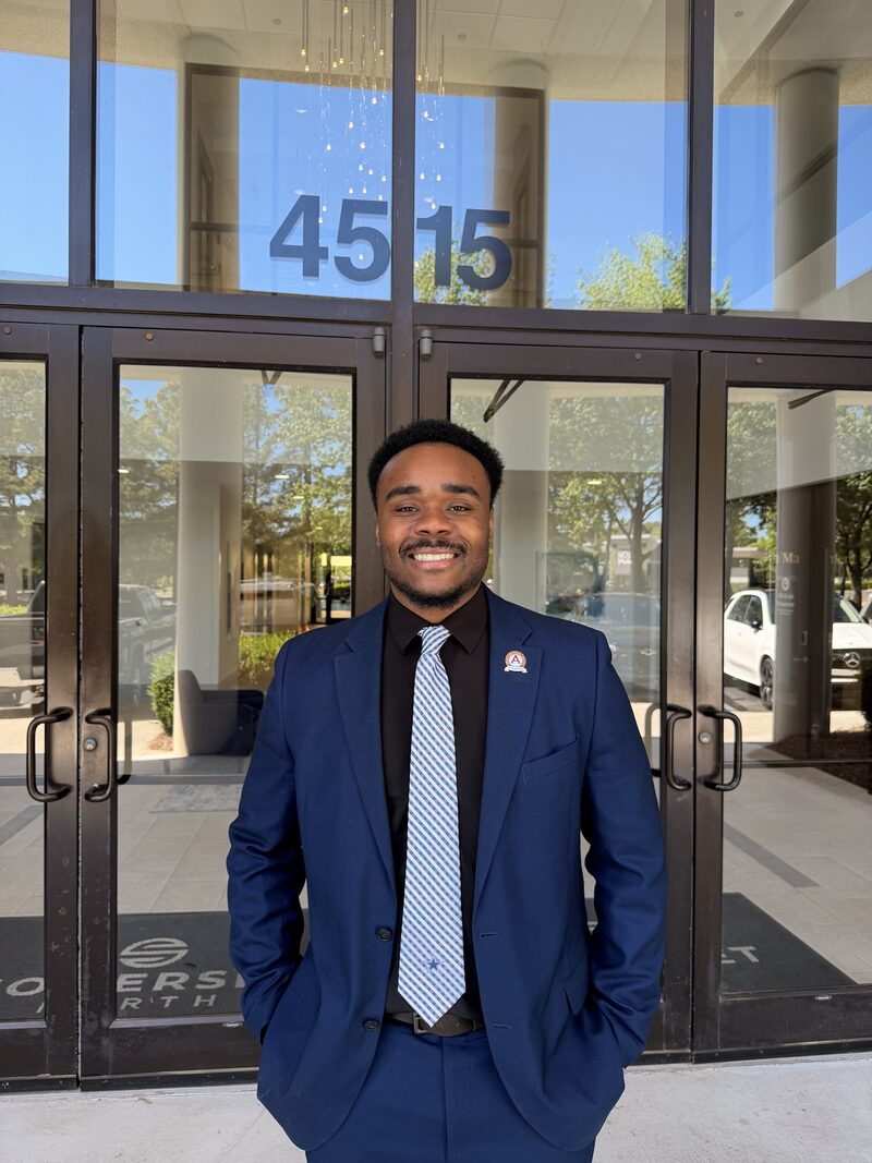 A confident Noble Impact Marketing team member in a navy suit outside an office