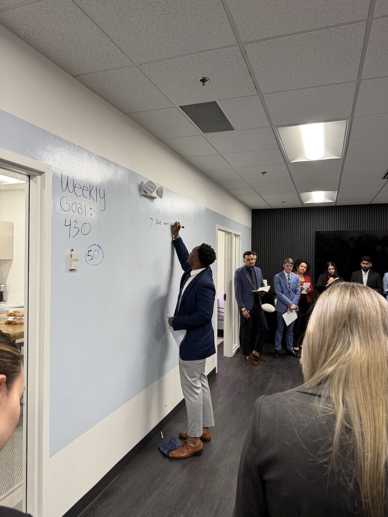 Team leader setting weekly goals on a whiteboard during a Noble Impact Marketing training session